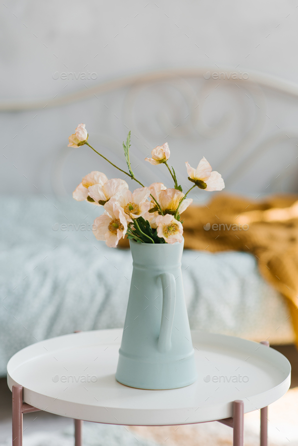 Artificial poppy flowers in a blue vase in the form of a jug on the coffee table in the interior