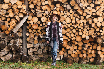 Beautiful woman wearing authentic handmade sweeter and brown hat stay near chopped woods wall.