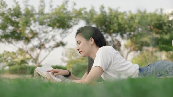 Attractive Asian teenage student reading and learning while lying on the floor grass outdoors.