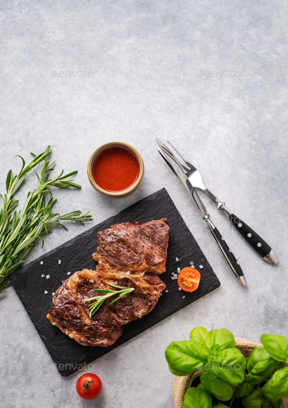 BBQ grilled beef steak with sauce, rosemary and basil on black slate on ...