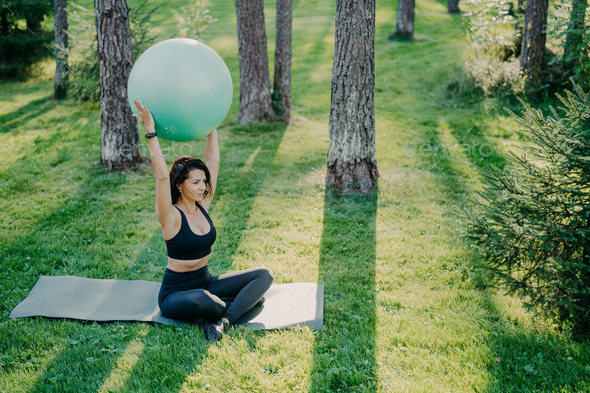 Fit sporty woman exercises with fitness ball sits on karemat in lotus pose