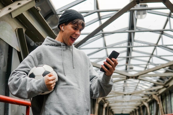 Young hipster man holding smartphone and celebrate win a bet. Soccer bet, sports gambling.