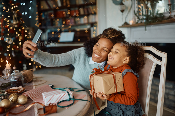 Cheerful black mother and daughter taking selfie on Christmas day at home.