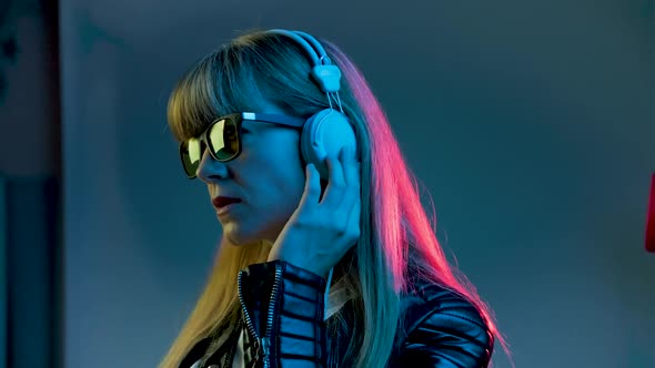 Woman with Headphones Listening to Music and Dancing in Neon Light at Studio alt