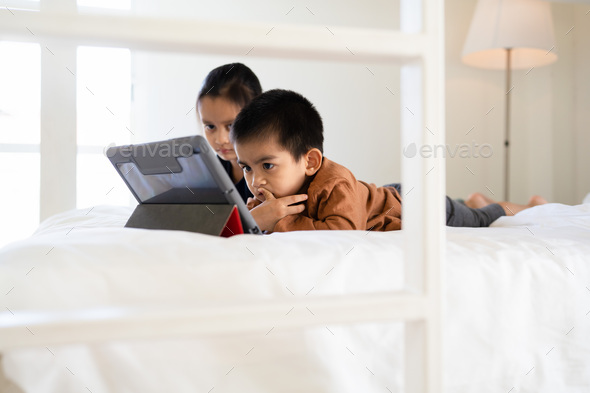 Asian little sibling watching video clip on tablet together in the bedroom.