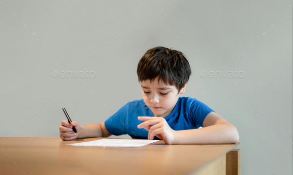 Kid siting on table doing homework,Child boy holding black pen writing on white paper