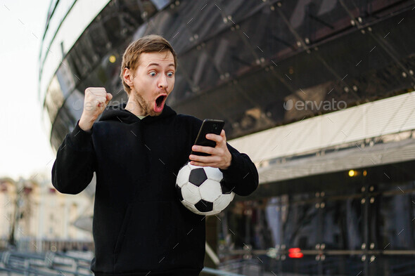 Young man holding smartphone and celebrate win a bet. Soccer bet, sports gambling.