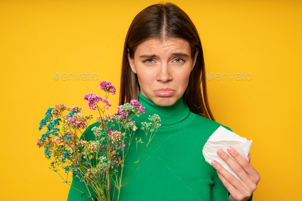Sad woman upset with having allergic reason to pollen holding tissue and bouquet of wild flowers