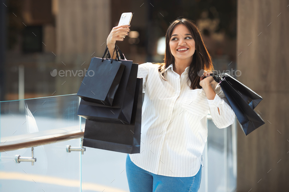 Lifestyle beautiful plus size happy woman make a picture on smartphone with purchases
