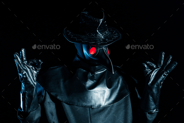 Man in plague doctor costume with crow-like mask meditating isolated on black background