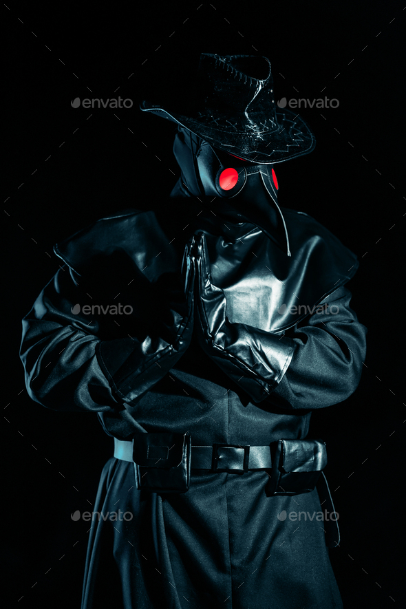 Man in plague doctor costume with crow-like mask praying with hands isolated on black