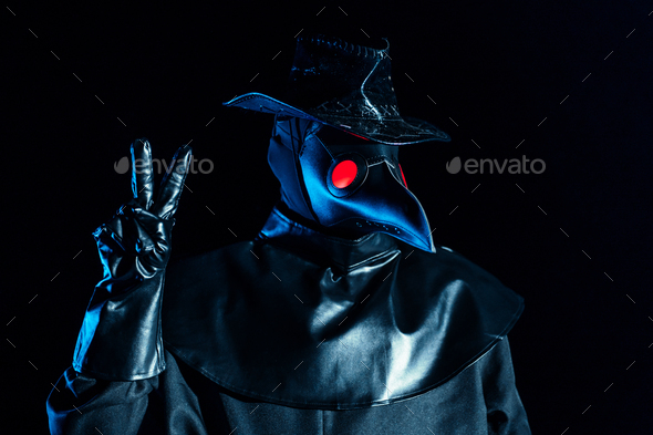 Man in plague doctor costume with crow-like mask showing peace gesture isolated on black