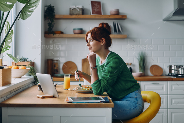 Beautiful young woman having lunch while sitting at the kitchen counter at home