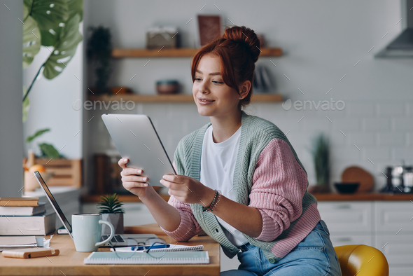 Beautiful young woman using digital tablet while sitting at the kitchen counter at home