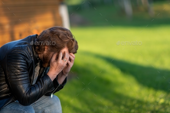 A sad young man crying hiding his face in his palms sits and thinks ...