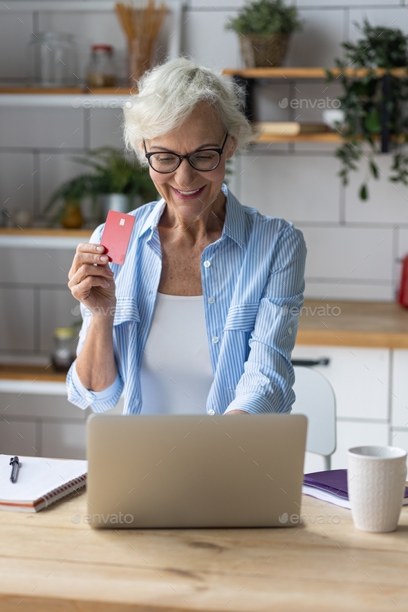 Beautiful senior woman with short grey hair and lovely smile doing shopping in the internet at home