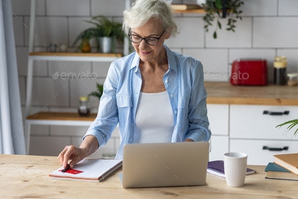 Beautiful senior woman with short grey hair and lovely smile doing shopping in the internet at home