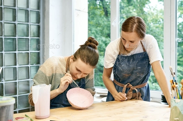 Young skillful pottery master teaching apprentice sculpting and painting mud bowl in art studio