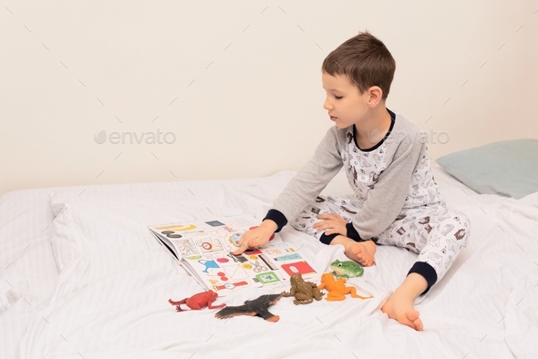 Child boy sits on the bed and reads a book to his toys. Relaxing at home concept.
