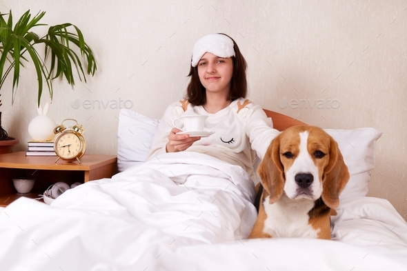 A young girl in bed with a cup of coffee and a dog beagle