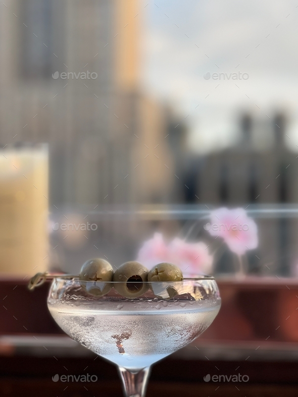 Martini with olives at a rooftop bar with the city in the background