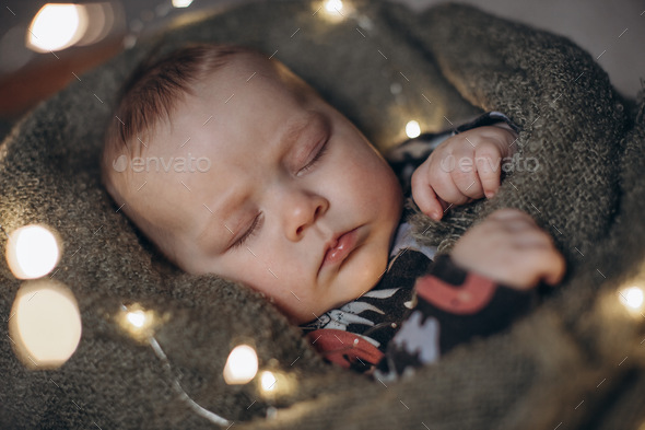 portrait of a sleeping baby in a warm blanket among the lights of a garland