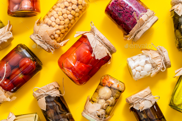 Various kinds preserves vegetables and mushroome in glass jars. Placed on yellow background - Stock Photo - Images