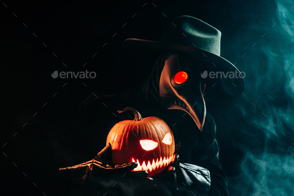 Plague doctor with pumpkin lantern on black smoke background. Creepy raven mask
