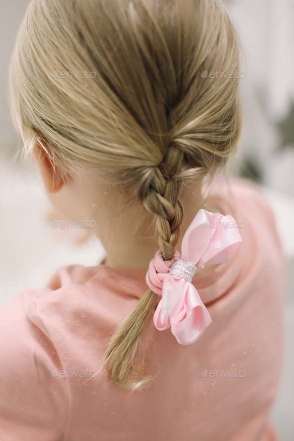 Blonde little girl braid hair with pink ribbon bow. Haircare, hairstyling.