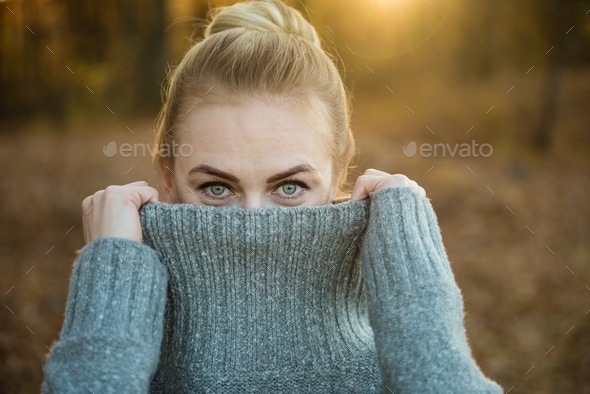 Woman covers part of her face with a sweater. He looks at the camera.