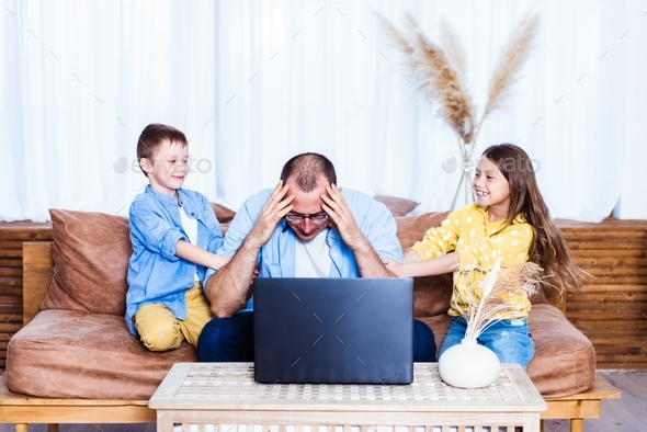 Work from home. Man in stress works on laptop with children playing around