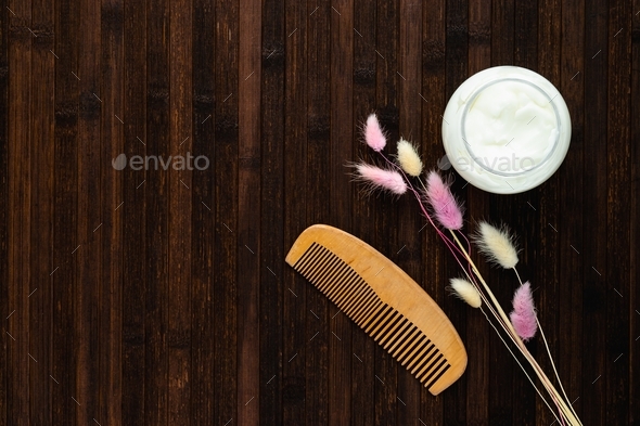 Ecological cosmetics. An open jar with a hair mask, a natural wood comb and dry flowers on a dark wo