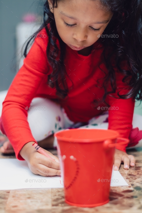A little girl dressed in red coloring with a red crayon