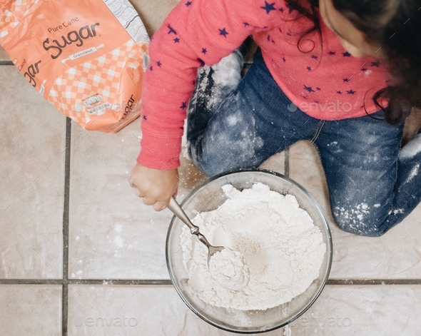 A toddler mixing a bowl of flour and sugar to cook pancakes