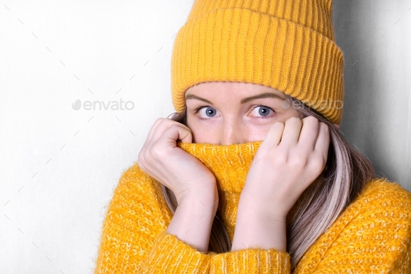 Young freezing woman is pulling her high neck sweater up