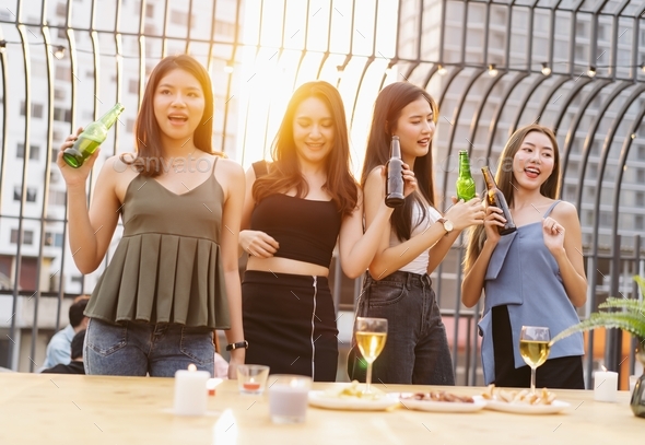 Asian Girls gang drinking beer while enjoying rooftop bar party. Group of friends having fun.
