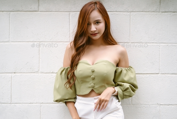 Sexy Asian woman wear green off-shoulders clothes and looking at camera standing white brick wall