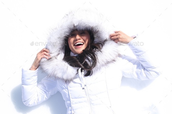 Happy female in a white warm winter coat laying in the white snow