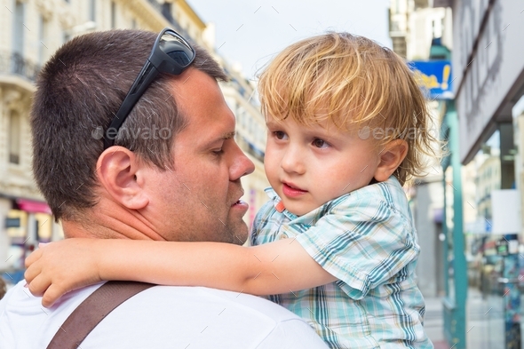 Father holds a tired child in his arms while walking around the city. Dad calming down his son.