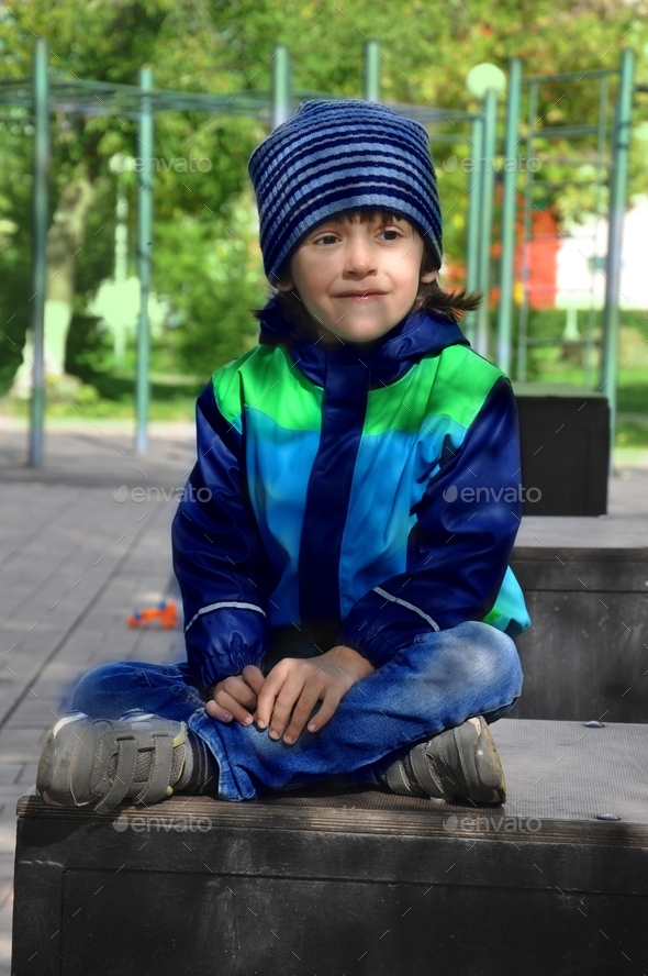 Cutie smiling boy sitting in park and looks straight ahead