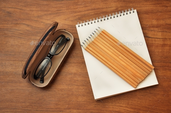 The top view flat lay of workspace. Eyeglasses in eyeglasses case and notepad with pencils