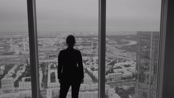 Business Woman Stands Near a Large Window on a High Floor of a Skyscraper alt