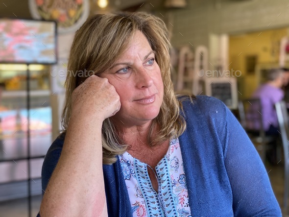A baby boomer woman in a restaurant sits and thinks about the future and hopes the pandemic will end