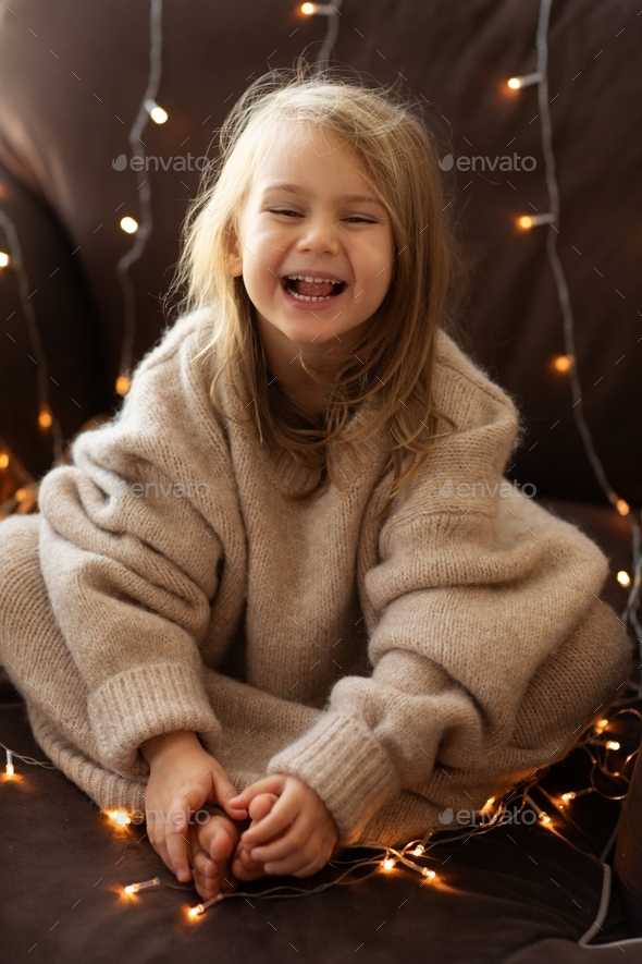Cozy vibes.Happy child bare feet in beige sweater and christmas lights.happy face