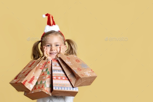 surprised happy child girl in Santa hat holding shopping gift craft paper bags presents