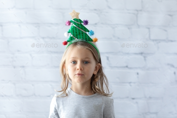 child girl in headband with a Christmas tree isolated white brick wall background.Happy new year