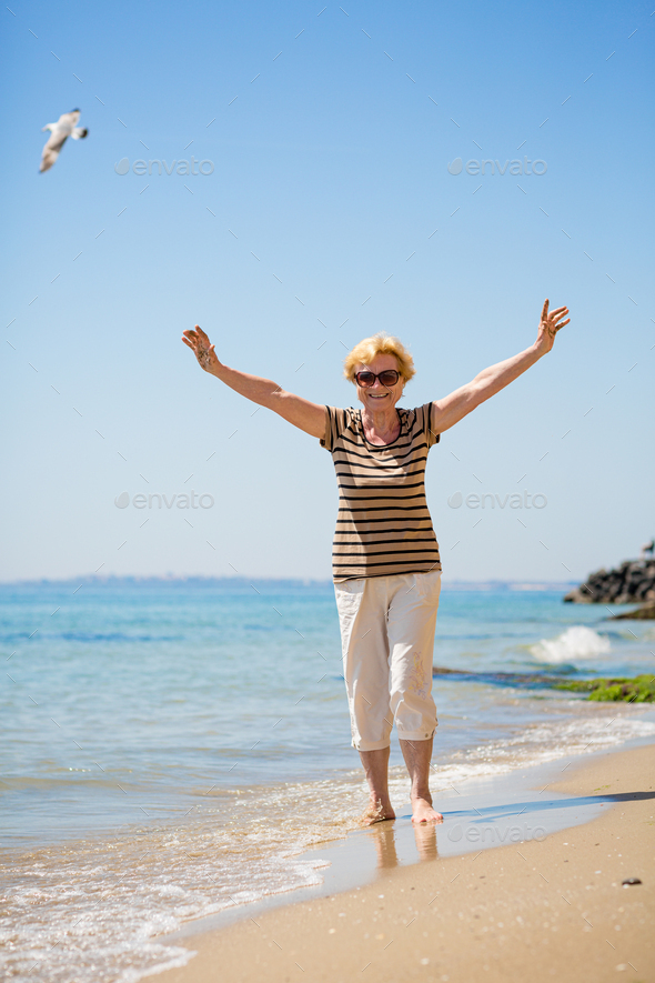 Elderly attractive woman walking along the beach and showing her palm hands
