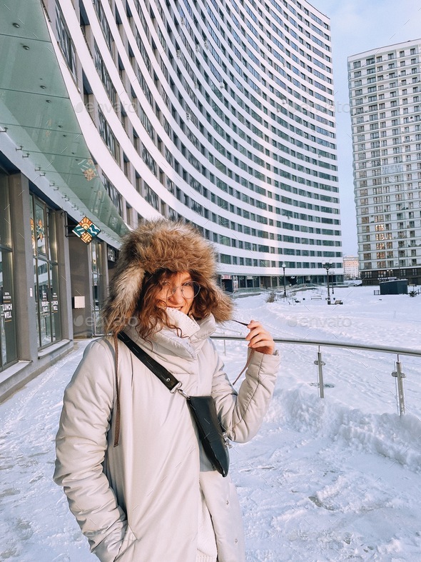 Girl wearing cozy winter clothes.Enjoy winter.Snowy weather.City  architecture. Apartment building Stock Photo by matskevichtanya