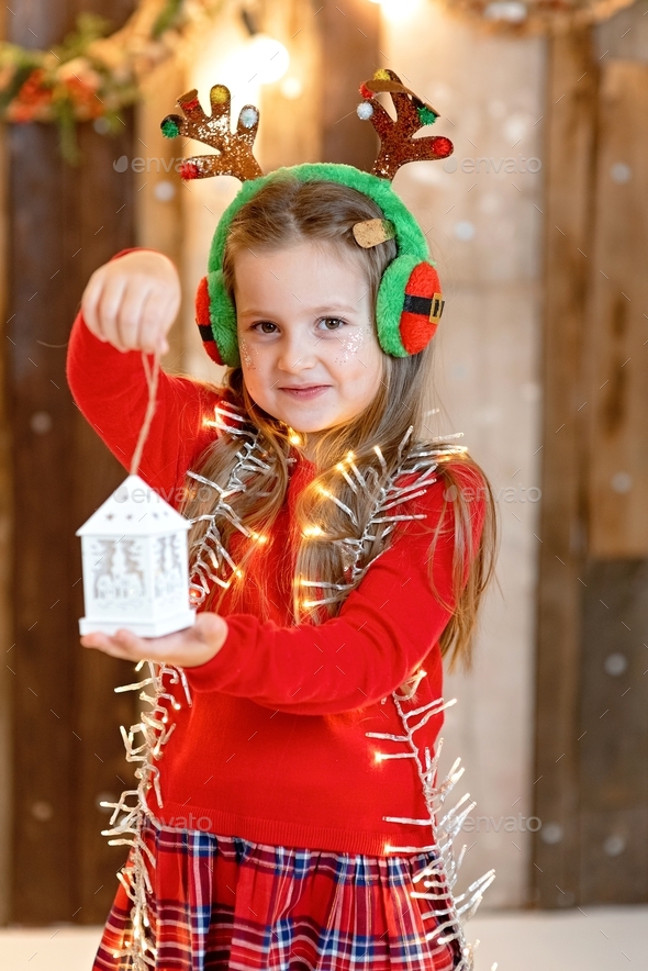 Happy smiling little girl holding Christmas lights and wearing fancy