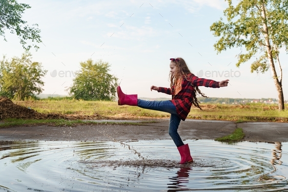 Child with rain boots run into a puddle. Happe childhood concept.